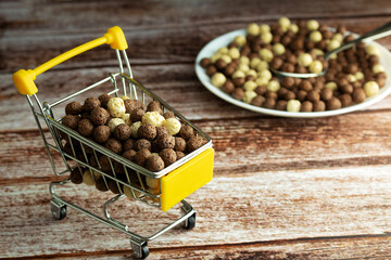 Corn balls, breakfast, chocolate flavored, in a shopping trolley, on a wooden background, front view, still life, bowl of balls