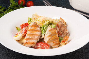 Caesar salad with chicken on a white plate on a black background