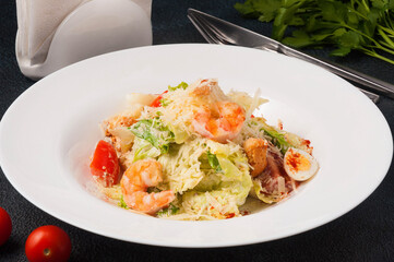 Caesar salad with shrimp on a white plate on a black background