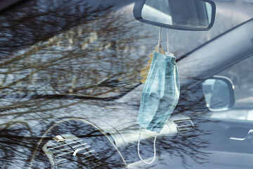 Face mask on the car mirror, real life with coronavirus, tree reflection in glass, horizontal photo