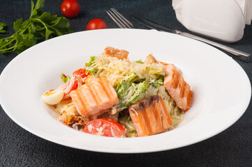Caesar salad with grilled salmon in a white plate on a black background