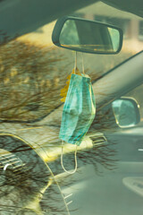 Face mask on the car mirror, real life with coronavirus, tree reflection in glass