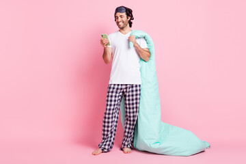 Full size photo of young happy smiling man hold blanket addicted to smartphone isolated on pink color background