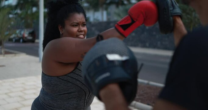 Curvy woman doing boxing exercise with her personal trainer outdoor - Sport and plus size people concept