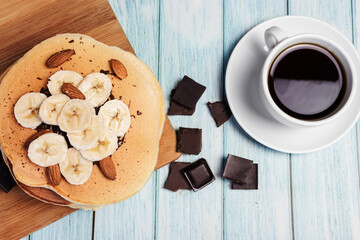 Pancakes with banana and nuts on a wooden board, blue light background, top view