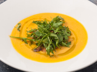cream of pumpkin soup with arugula on a white plate