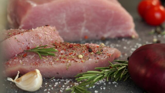 Close up of fresh raw pork is sprinkled with peppercorns, spices and seasonings on background of vegetables. Food concept, cooking meat steak.