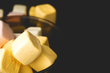 Yellow marshmallow square shape in a bowl on a dark background, front view, still life