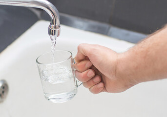 tap water is poured into a glass cup held by a man's hand.