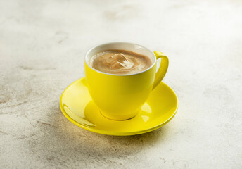 Yellow cup with cappuccino coffee on a light background.