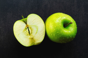 Green apple on a dark background, water drops on an apple, apple in a cut, green skin, healthy food, vitamins, top view in a close-up