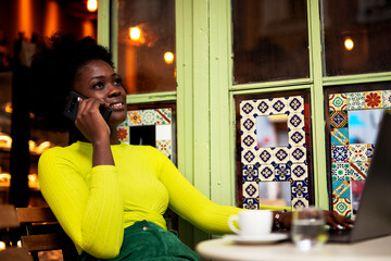 Businesswoman talking to the phone in cafe. African woman with laptop in coffee shop