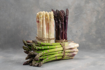 Three bunches of different fresh asparagus isolated on grey. Purple white and green asparagus.