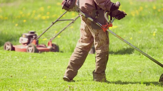 Professional gardener mowing lawn at central park property with gasoline brush cutter. Sunny day