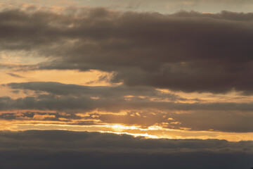 A yellow, blue sunset with thick clouds in the sky before a storm with a dark meadow and tree horizon on a spring evening. The sun is not visible