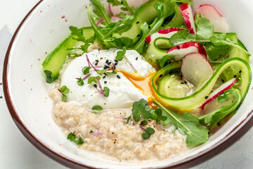 Breakfast oatmeal porridge with oatmeal porridge, poached egg with vegetable salad of radish, cucumbers, arugula and microgreens. balanced food. Food recipe background. Close up