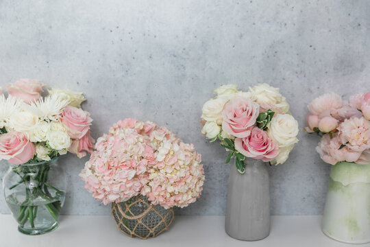 Several rose, peony and hydrangea flower arrangement bouquets against a horizontal concrete wall