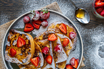 French toast with fresh raspberries, strawberries, maple syrup, and sugar powder on a plate. Tasty morning breakfast or brunch with gluten free bread. Easy making and healthy dessert. Top view