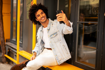  Young man enjoying outdoors. Handsome man with curly hair using the phone, having video call.