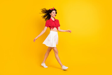 Full size profile photo of cute optimistic brunette hair lady go wear red top skirt sneakers isolated on yellow color background