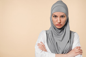 Offended sad angry with negative emotions young middle eastern arabian muslim islamic woman in grey hijab isolated over beige background. Feeling bad, disappointed, break up, quarreling, blowing lips