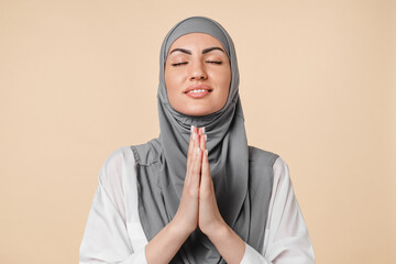 Praying hoping young Middle Eastern arabian muslim islamic woman in grey hijab asking begging for help, prayer mosque isolated on beige background. Hopeful parishioner