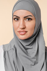 Image of a young beautiful arabian muslim islamic Middle Eastern woman in grey hijab isolated over beige background. Woman in scarf nice-looking girl advertisement, cutout