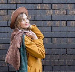 Naklejka premium Young woman holding a brown eco textile bag with space for mockup. Dressed in a yellow coat, hat, scarf. The concept of ecology or environmental protection. Ecological shopping. Style and fashion.
