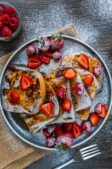 French toast with fresh strawberries, raspberries, maple syrup, and powdered sugar on a plate. Tasty morning breakfast or brunch with gluten free bread. Easy making and healthy dessert. Top view