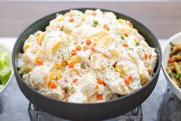 Creamy potato salad in a black bowl; assorted fresh salad displayed on a buffet in individual containers at restaurant.