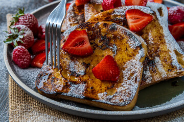 Eating french toast with fresh strawberries, raspberries, maple syrup, and powdered sugar using a fork. Tasty morning breakfast or brunch with gluten free bread. Easy making and healthy dessert. 