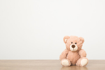 Smiling brown teddy bear sitting on wooden table at light gray wall background. Closeup. Front...