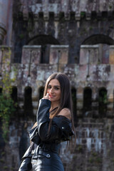 Fototapeta premium portrait of pretty young brunette woman dressed in a leather jacket in front of an old castle