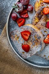 French toast with fresh strawberries, raspberries, maple syrup, and powdered sugar on a plate. Tasty morning breakfast or brunch with gluten free bread. Easy making and healthy dessert. Top view