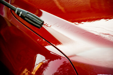 Washing a red car with high pressure washer cleaner.