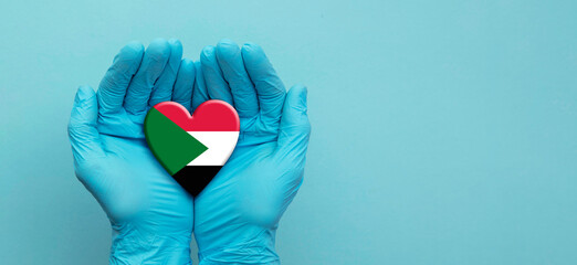 Doctors hands wearing surgical gloves holding Sudan flag heart