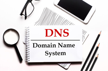 On a white background glasses, a magnifier, pencils, a smartphone and a notebook with the text DNS...