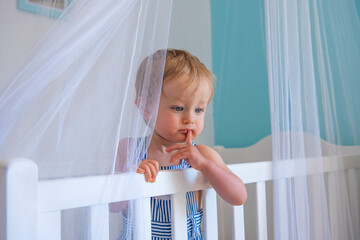 portrait de bébé garçon debout dans son lit à barreaux