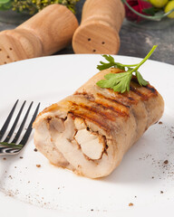 grilled chicken roll decorated with greens on a white plate