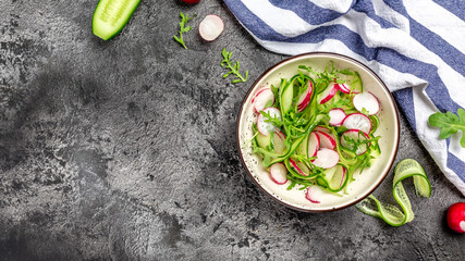 Fresh radish salad with cucumbers and arugula on dark background. Spring summer vegetable salad. Long banner format, top view