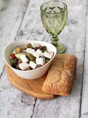 Mediterranean cuisine concept. Greek salad in white bowl and glass of water on the wooden background.