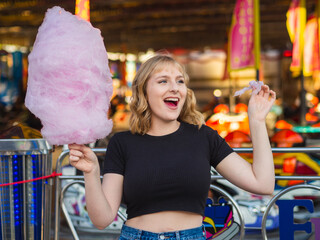 Mujer guapa y joven comiendo algodón de azúcar en la feria 