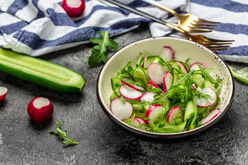 Fresh radish salad with cucumbers and arugula on dark background. Spring summer vegetable salad. Healthy balanced food. banner, menu recipe place for text, top view