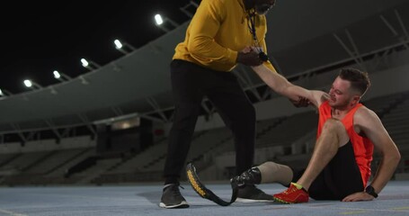 Diverse male coach helping tired disabled male athlete with running blade to stand up - Powered by Adobe