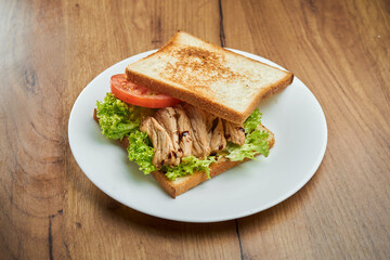 Delicious snack - toast sandwich with grilled chicken, tomatoes and sauce in a white plate on a wooden background
