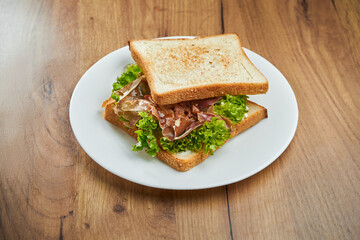 Delicious snack - toast sandwich with sun-dried tomatoes and jamon, sauce in a white plate on a wooden background
