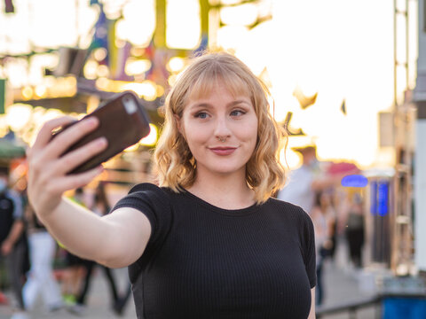Mujer joven haci&eacute;ndose un selfie en una feria o parque de atracciones durante la puesta de sol 