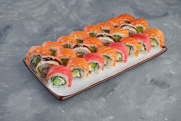 Appetizing set of sushi rolls Philadelphia in red tobiko caviar with salmon, tuna and eel in a white plate on a gray background. Japanese food