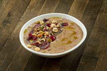 Appetizing flaxseed porridge with olive oil, seeds, grapes and hazelnuts in a white bowl on a wooden background. Vegetarian food. Eastern cuisine