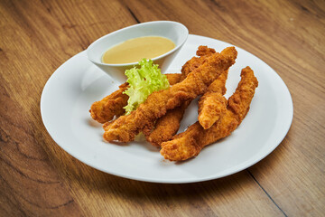 Deep-fried, breaded chicken nuggets, served in a white plate with honey mustard sauce in a white plate